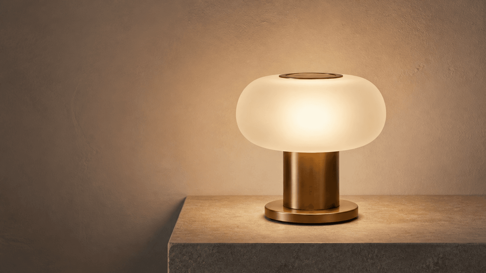 Warm sculptural table lamp on a minimal textured interior surface.